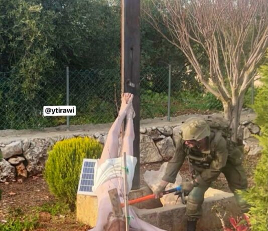 Soldado israelense fardado usando uma marreta para destruir a cabeça de uma estátua de Jesus Cristo caída no chão em um jardim no sul do Líbano.