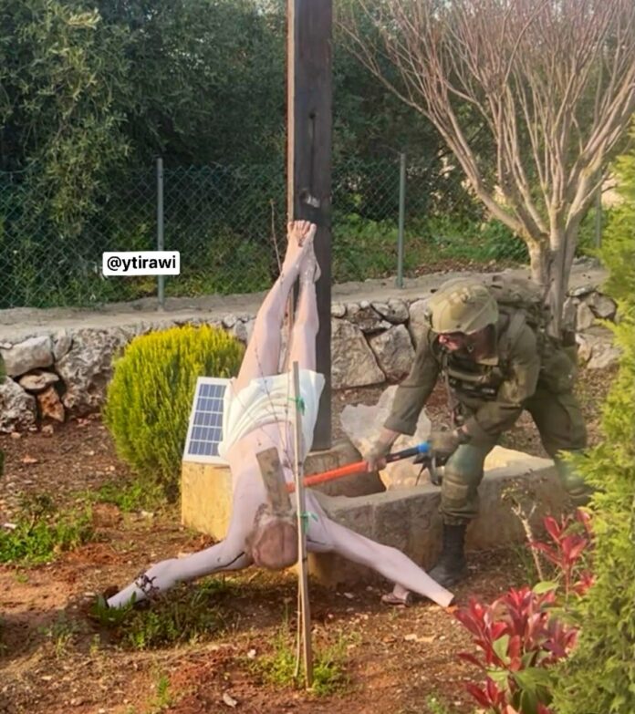 Soldado israelense fardado usando uma marreta para destruir a cabeça de uma estátua de Jesus Cristo caída no chão em um jardim no sul do Líbano.